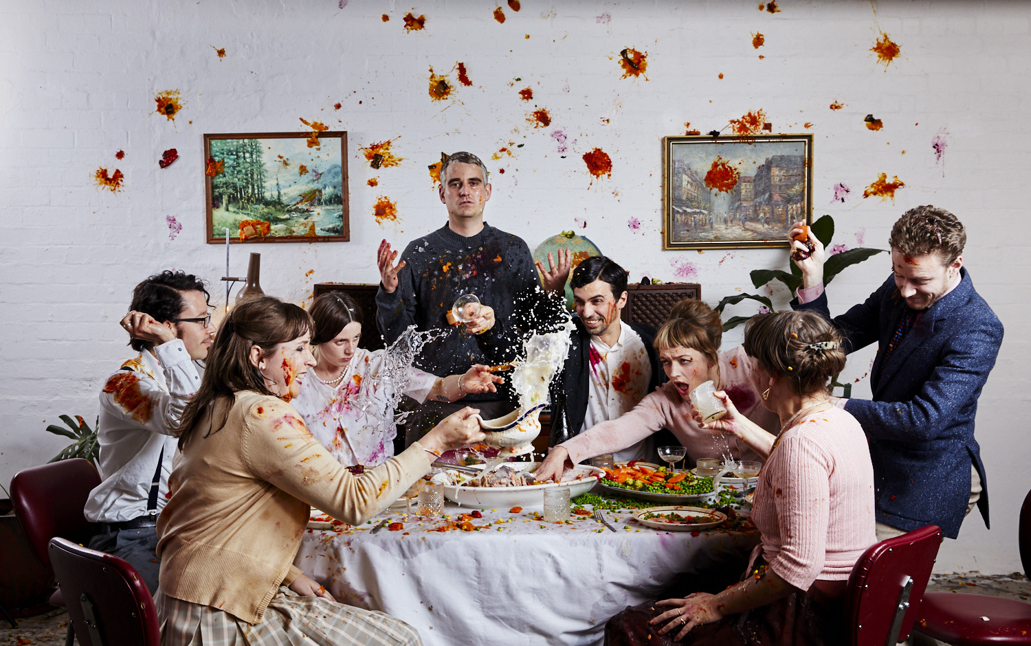 A scene depicting Markj standing behind a dinning table with his guests having a food fight.